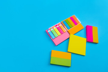 Several colored sets of stickers in yellow, pink, orange with stickers in the form of pencils and stripes located on the side on a blue background. Close-up. Sets for notes. Stationery.