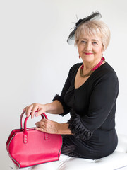 Fashionable elderly woman in a black dress and a hat with a red leather bag in her hands on a white background
