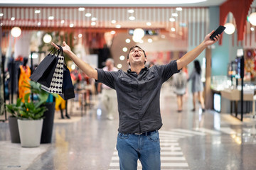 Happy young man posing holding a large number of packages with shopping in a raised hand, in the...