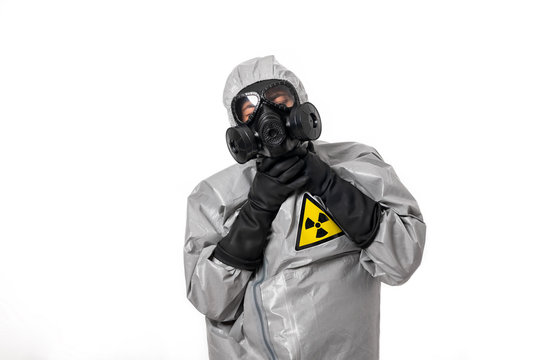 A man in a gray protective suit with a hood on his head with a yellow radiation sign, with a protective gas mask, posing, holding on to his throat. Choking environment. 
