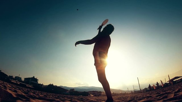 Silhouette of young men play ball paddle beach or tennis on the sand in the shore of the beach