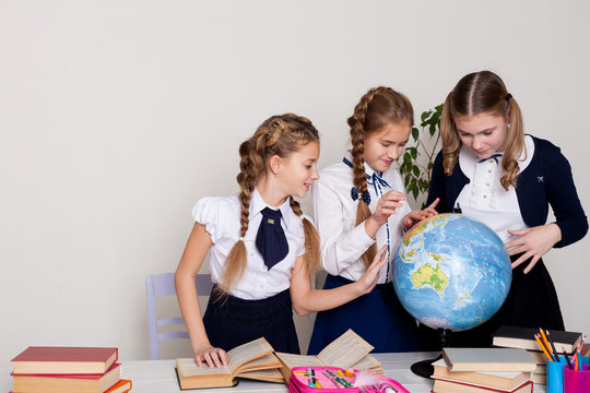 three schoolgirls at the desk study the globe in a geography class