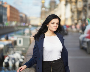 Portrait f beautiful intelligent brunette who walks down street of Saint-Petersburg in city center. Charming thoughtful woman with long dark hair wanders alone, immersed in thoughts