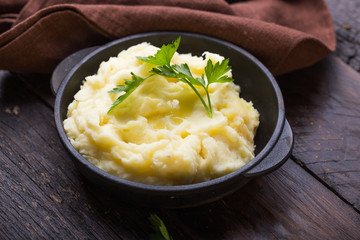 Mashed potatoes or boiled puree with parsley  in cast iron pot on dark wooden rustic background.  top view..