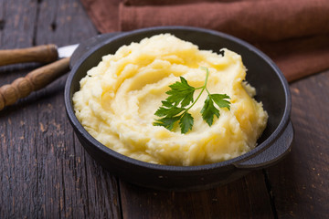 Mashed potatoes or boiled puree with parsley  in cast iron pot on dark wooden rustic background. ...