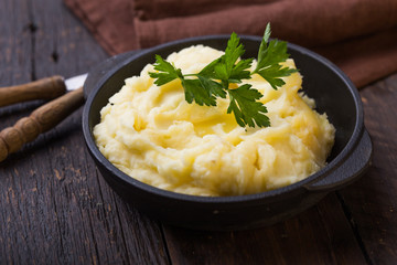 Mashed potatoes or boiled puree with parsley  in cast iron pot on dark wooden rustic background. ...