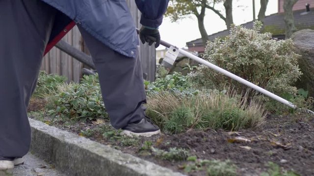 Gardening leisure activity. Gardener raking soil preparing for new vegetation & clearing weeds. Pull back low angle.