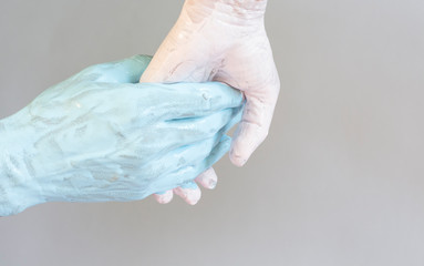 Male and female hand in blue and pink paint holding each other