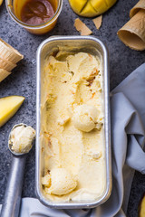 Close up bowl with vanilla ice cream covered with caramel sauce and fresh mango fruit on dark background. Selective focus. Summer dessertz
