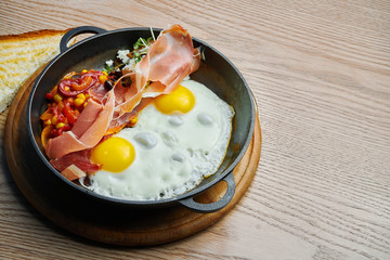 Fried eggs with prosciutto, beans and chili peppers and corn in tomato sauce served in a mini skillet. Tasty food for breakfast