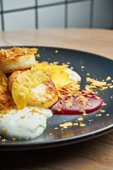 Homemade cheesecakes or Syrniki with jam, pumpkin and sour cream on a black plate on a wooden background. Ukrainian food. Breakfast food