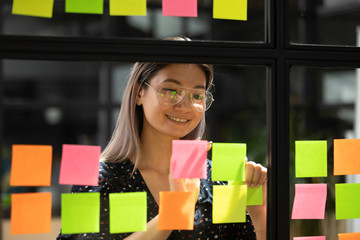 Asian businesswoman attached on glass sticky notes writes creative ideas