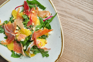 Close up view on tasty Light salad with prosciutto, a mix of greens, pineapple and blue cheese in stylish grey bowl.