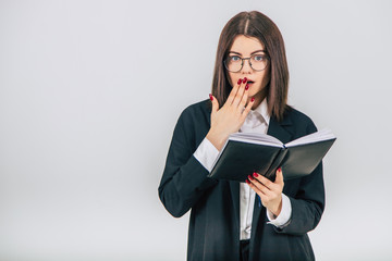 Successful young businesslady checking data in her notebook, thinking, covering mouth, shocked face expression.