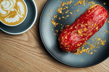 Appetizing and large eclair with glaze of raspberry on top and fir cream inside on a black plate....