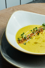 Creamy cream soup in a beautiful bowl with crackers, fried bread and microgreen. Tasty food for lunch. wooden background