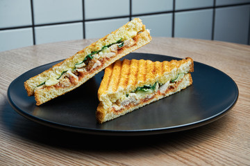 Close up Juicy and nutritious sandwich with turkey and pineapple, cheese and lettuce on black plate on wooden background.