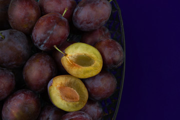 Fresh organic plums in glass vase isolated on blue background. Still life of ripe and juicy fruits