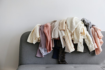 Categorizing winter laundry concept. A messy pile of kniwear lying on grey textile sofa. Bunch of...