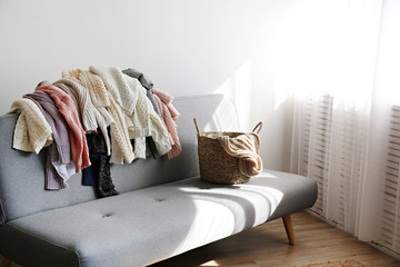 Categorizing winter laundry concept. A messy pile of kniwear lying on grey textile sofa. Bunch of unfolded sweaters prepeared for sorting. Close up copy space, background.