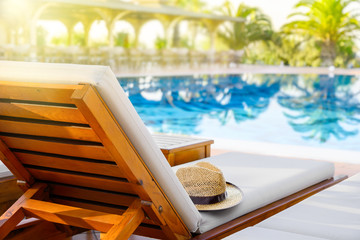 Lounger with sun hat and swimming pool in luxury resort - obrazy, fototapety, plakaty