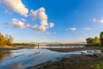 The destroyed bridge over a wide river. Autumn by the river. Beautiful cumulus clouds in a clear blue sky. Nature. Scenery.