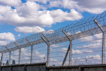 Obraz premium Slatted fence with barbed wire on top. Cloudy sky behind the fence. imprisonment concept.