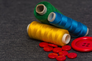 Colorful bright threads for sewing and red buttons. Gray blurred background. Sewing industry. Atelier design elements.