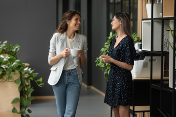 Asian and Caucasian ethnicity women colleagues chatting in office hallway
