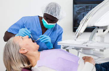 Mature female patient sitting in dental chair. Dentist is treating female patient
