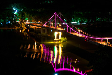 A bridge with multi-colored lights at night. A bridge over a wide river. Pedestrian bridge with purple lights