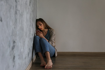 Portrait of beautiful young woman with depressed facial expression sitting in the corner holding...
