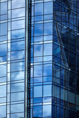 Fototapeta na wymiar Windows of a skyscraper with reflection of blue sky and white clouds. A fragment of a glass facade of a modern office building in a business district of a city. Geometric shapes in modern architecture