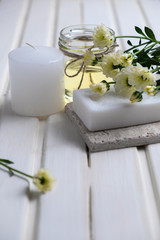 Handmade soap with a pattern lies on the table.  On a white table is handmade soap, flowers and olive oil.  Collection of items for the bathroom