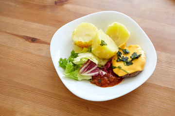 Boiled potatoes with green salad, vegetables and cutlet. Plate with homemade food on a wooden dinner table. Cooked potato dish
