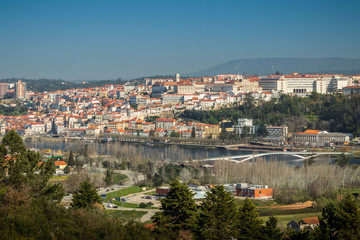 View of the city of Coimbra in Portugal, from downtown to high with the University, also with the Mondego river and the pedestrian bridge Pedro e Inês in the foreground.