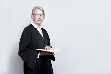 Female lawyer concept: mature woman in a black gown holding a legislative text book, copy space.