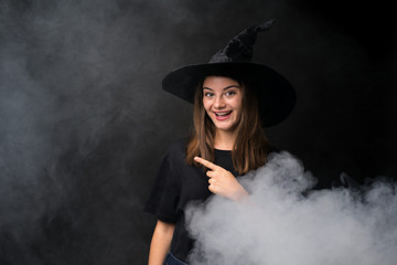 Girl with witch costume for halloween parties over isolated dark background pointing finger to the side