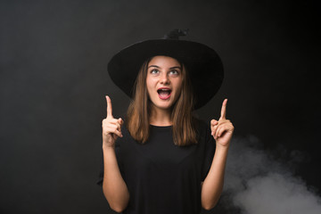 Girl with witch costume for halloween parties over isolated dark background pointing with the index finger a great idea