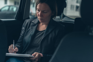 Businesswoman doing paperwork in car at the back seat