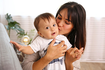 Portrait of young mother taking care of her little son at home. Beautiful female with straight brunette hair playing with child at living room. Close up, copy space, background.