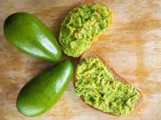 Top view on cut board with two avocado and sandwiches with guacamole 