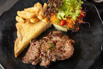Beef steak grilled until cooked served with garlic bread, french fries and fresh vegetable salad, everything is placed on a matt black plate. Complete with useful nutrients suitable for a good meal