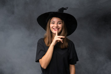 Girl with witch costume for halloween parties over isolated dark background doing silence gesture
