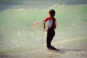 Boy with surfboard entering the sea