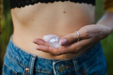 Female hands holding two yoni eggs for vumfit, imbuilding or meditation are made from pink quartz and transparent violet amethyst over her naked tummy outdoors