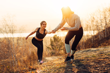 Young women jogging in nature. Girlfriend helps her friend climb the slope.