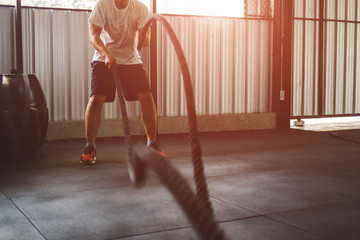 Athletic men doing a fitness workout with battle rope in functional training fitness gym. men With...