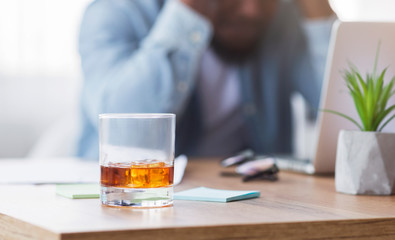 Desperate black businessman suffering from bankruptcy, drinking alcohol at workplace.
