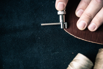 the tanner makes markings for punching on a brown leather workpiece using a special tool on the...